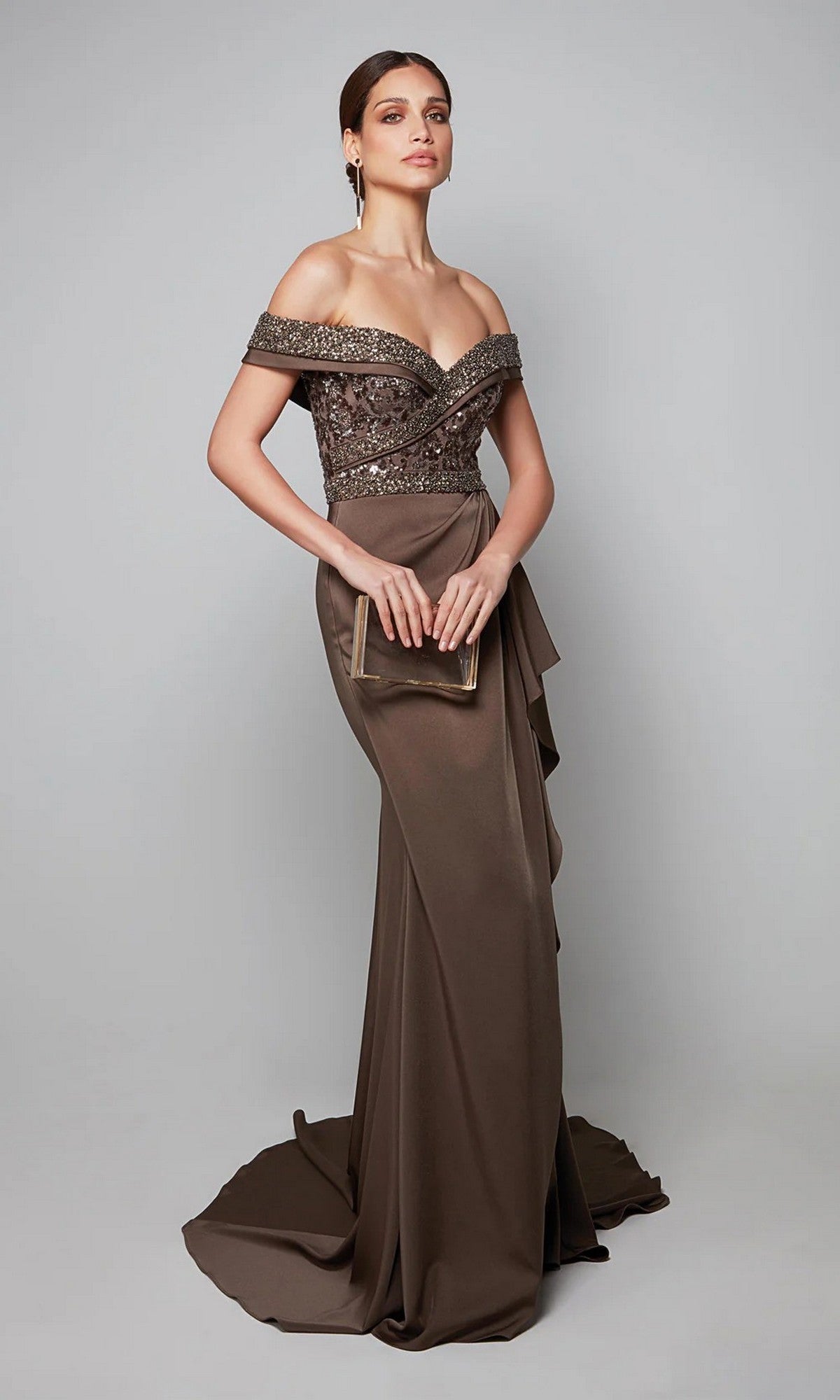 A woman in the Alyce 27619 long formal dress featuring an off-the-shoulder, beaded bodice gown holds a matching clutch while standing against a plain gray background.